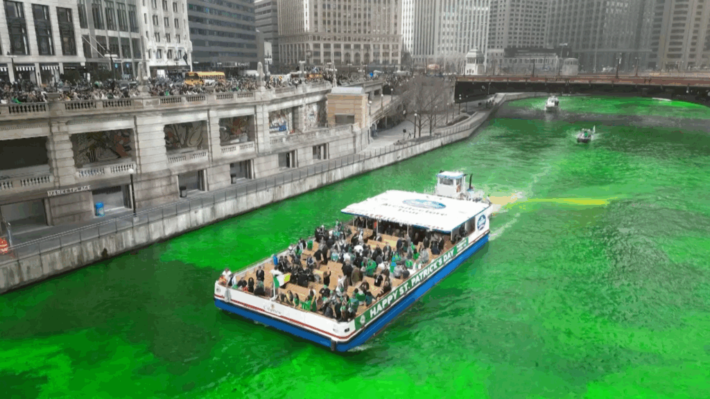 A high-resolution aerial photo of the green Chicago River surrounded by skyscrapers.